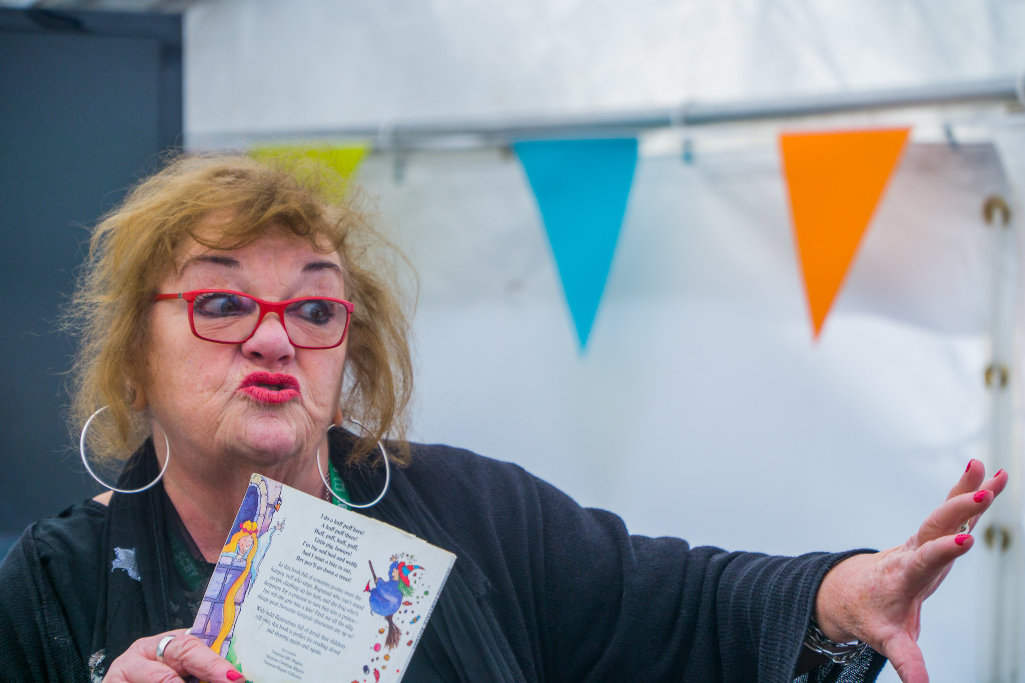 A woman holds a book and makes a dramatic expression and wave of the hand.